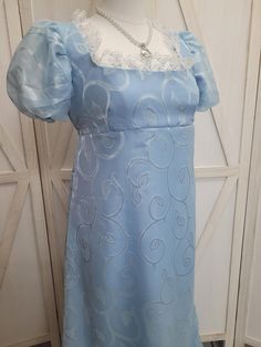 Bridgerton blue is always in style!  We offer a basic Regency styled gown, with the empire waist and short puffed sleeves.  This stunning dress is made with a light blue and a sheer blue swirling leaves overlay.  The neckline has been trimmed with white lace.  Dress is fully lined.    *This gown ties at the back with ribbons which can adjust the fit.      * All seams have been finished and this gown is spot clean or dry clean only.   If you have any questions about this dress, or any of our listings, please convo us before purchasing.  This listing is for the dress only, and jewelry shown is not included.  Thank you! Measurements:   Bust: 36-40"  Underbust: 34-36" Dress Underbust to Hem: 45" Hips: 50" Biceps: 12.5" (these are NOT elastic cuffs) Shoulder to underbust: 10.5"  Side to high Wa Daphne Bridgerton Dress, Bridgerton Blue, Bridgerton Daphne, 1800s Dresses, Jane Austen Emma, Daphne Bridgerton, Dresses Light Blue, Regency Dress, Womens Costumes