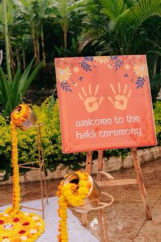 welcome to the haldi ceremony with hand prints and garlands on display in front of an orange sign