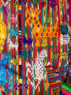 a colorful wall hanging with many different colored ribbons on it's sides and an assortment of other items in the background