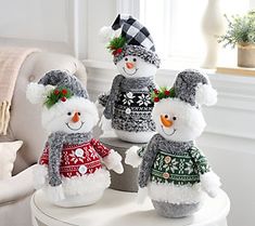 three snowmen wearing sweaters and hats sitting on a table