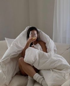 a woman sitting on a bed with a glass of wine in her hand and she is covered by a blanket