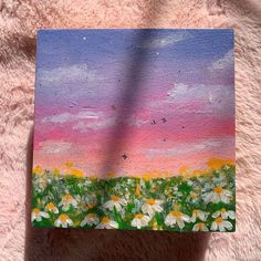 a painting of daisies in a field with pink and blue sky behind it on a furry surface