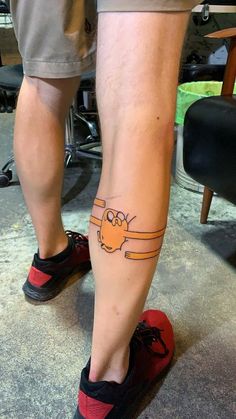 a person with a cartoon character tattoo on their leg, standing next to a chair