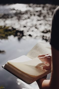 a person is holding an open book and looking at the water in front of them