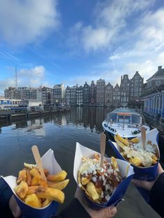 two people are holding containers with food in them near the water and boats on the water