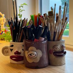 two mugs with faces painted on them are sitting on a table in front of a window