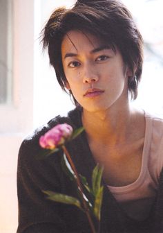 a young woman holding a flower in her right hand and looking at the camera with an intense look on her face