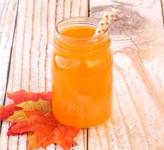 a glass jar filled with orange liquid next to an autumn leaf on a wooden table