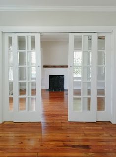 an empty room with wood floors and white doors leading to the living room, fireplace