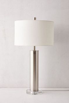 a lamp that is on top of a white table next to a wall with a light in it