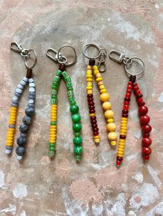 four key chains with beads on them sitting on a stone surface in front of a rock