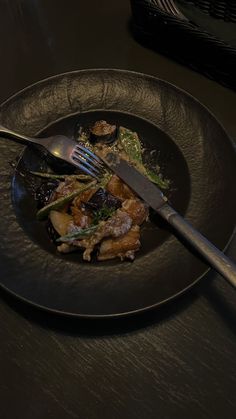 a black plate topped with food next to a knife and fork on top of a table