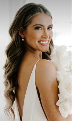 a woman in a white dress holding a bouquet of flowers and smiling at the camera