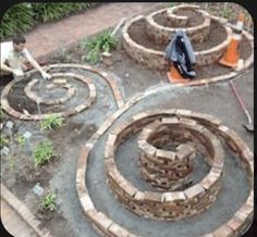 two men are working in the garden with bricks and brickwork around them, while another man is using a wheelbarrow