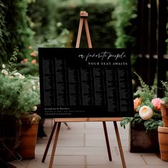 a black and white wedding seating plan on an easel in front of potted plants