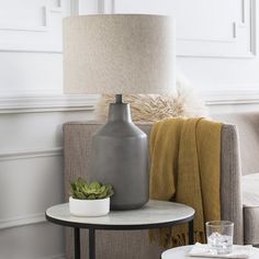 a table with a vase and a plant on it in front of a chair next to a lamp