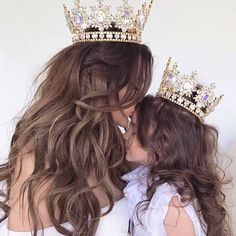 two women wearing tiaras kissing each other in front of a white wall with long hair