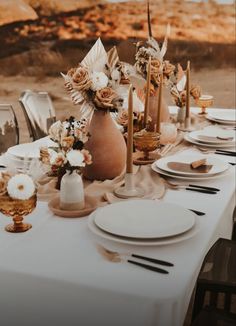 the table is set with plates, silverware and flowers in vases on it