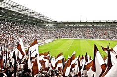 a large stadium filled with lots of people holding up white and brown flags in front of a green field