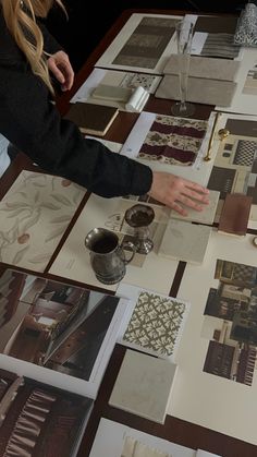 a woman is working on some art work at a table with pictures and other items