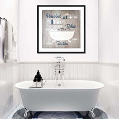 a white bath tub sitting next to a toilet under a framed art print on the wall