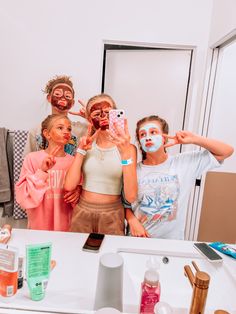 four people standing in front of a mirror with their faces painted like they are taking selfies