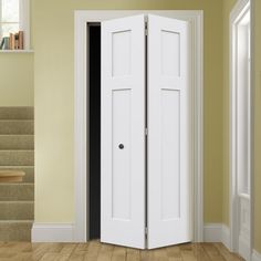 an open white door in the corner of a room with stairs and bookshelves