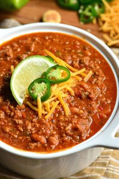 a white bowl filled with chili and cheese next to a lime slice on the side