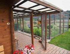 an outdoor area with flowers and plants on the ground near a wooden structure that has metal mesh fencing around it