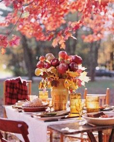 an outdoor table set with plates, glasses and vases filled with fruit on it