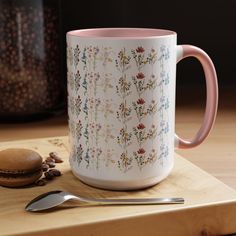 a white and pink coffee mug sitting on top of a wooden cutting board next to a spoon