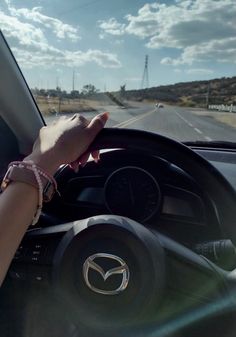 a person driving a car on the road with their hand on the steering wheel while wearing bracelets