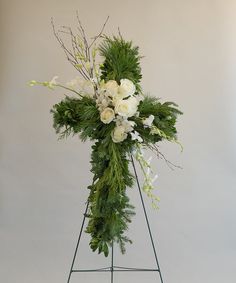 a cross with white flowers and greenery on it in front of a gray background