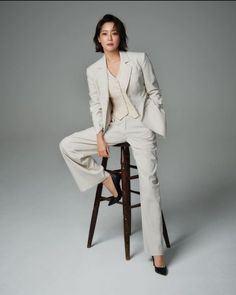 a woman sitting on top of a wooden stool wearing a white suit and black shoes