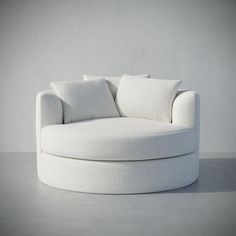 a white round couch with pillows on it's back and sides, sitting in front of a gray wall