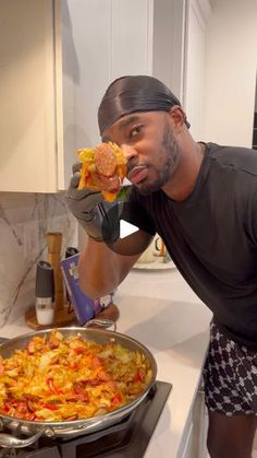 a man in black shirt and bandana eating food from a pan on stove top