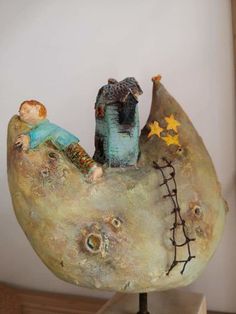 a ceramic sculpture of a man sitting on top of a moon with a small house