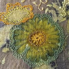 two yellow and green flowers on a table cloth with some thread in the middle, next to each other