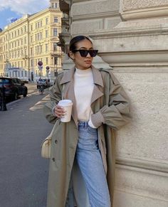 a woman leaning against a wall holding a coffee cup