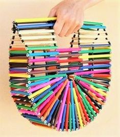 a hand holding a colorful purse made out of colored pencils