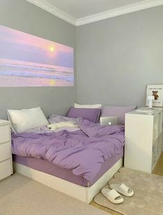 a bed with purple sheets and pillows in a bedroom next to a painting on the wall