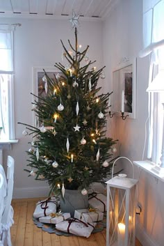 a small christmas tree in a room with white lights and presents on the floor next to it