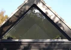 a triangle shaped window in the roof of a house with trees and bushes behind it