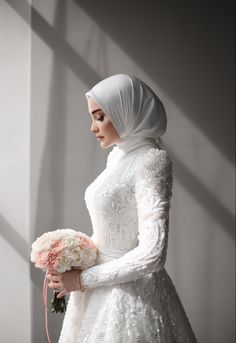 a woman in a white wedding dress holding a bouquet and wearing a hijab