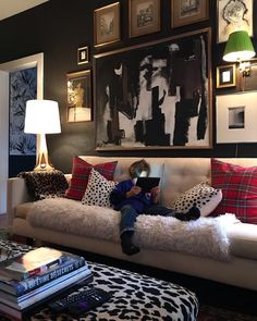 a person sitting on a couch in a living room with many pictures hanging above it