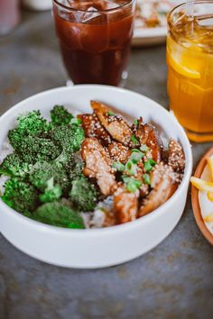 a bowl of broccoli and other food on a table next to two drinks