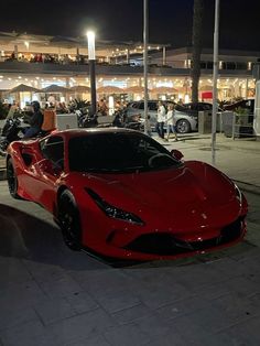 a red sports car parked in front of a building with people walking around it at night