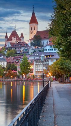 the city is lit up at night by the water's edge with lights reflecting in the water