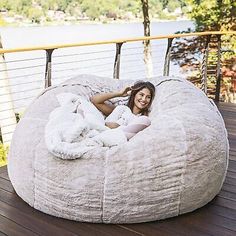 a woman laying on top of a large bean bag chair next to a body of water