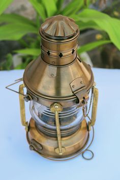 an old fashioned brass lantern sitting on top of a white table next to green plants